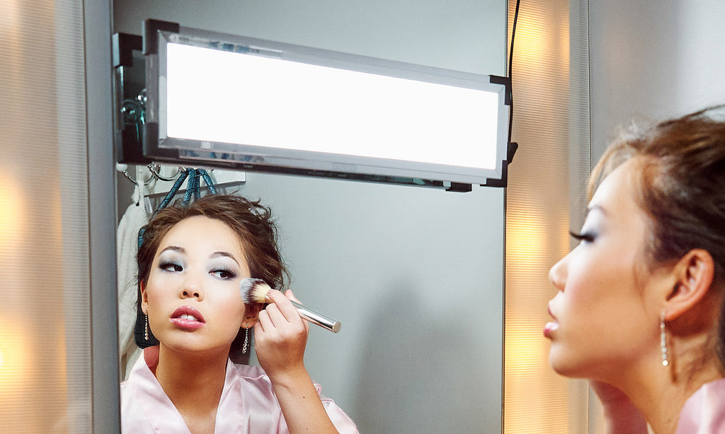 A woman adjusts her makeup in front of a mirror with an Eyelight Magic Kit on it