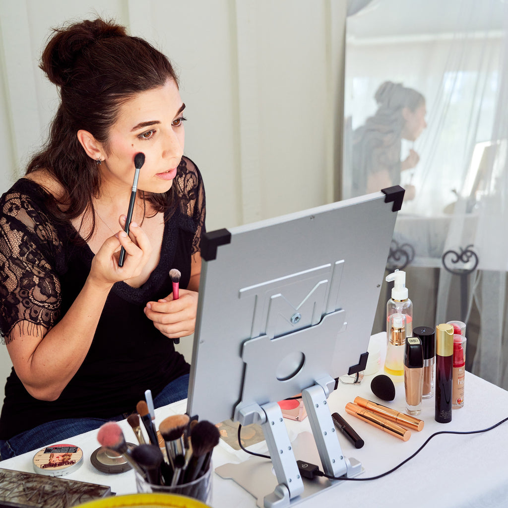 A woman sits at a table covered in makeup and a TML Meira makeup vanity
