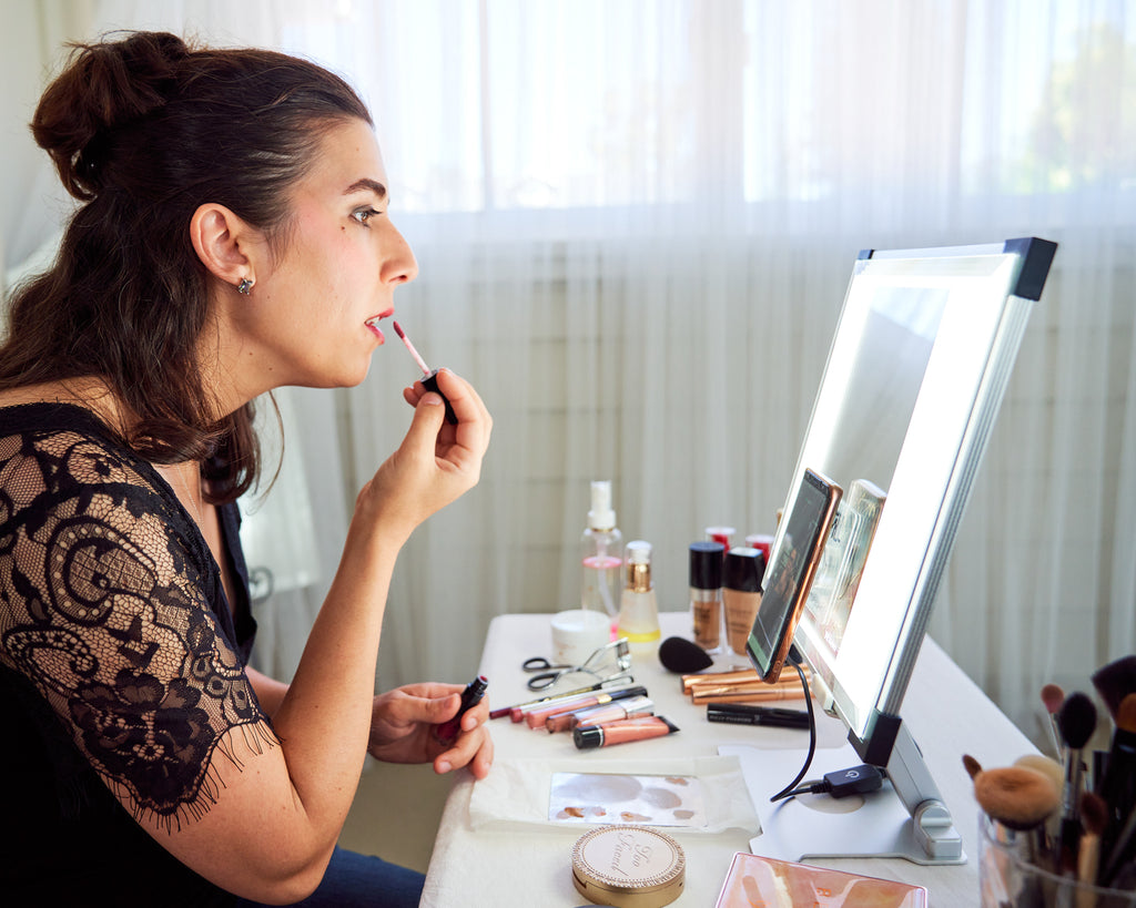 A woman applies lip gloss in front of TML Meira lighted mirror makeup vanity