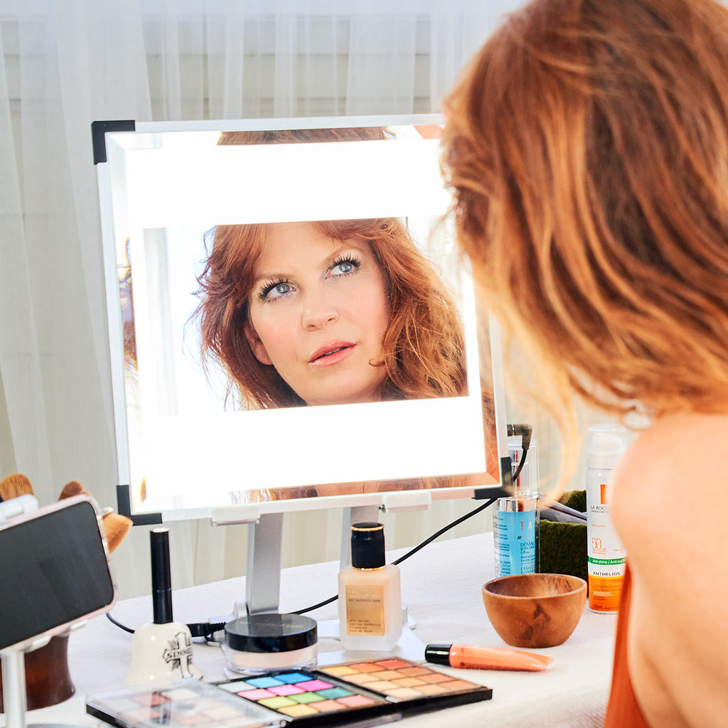 A red-headed woman looks at her reflection in her TML Meira with makeup products beneath it