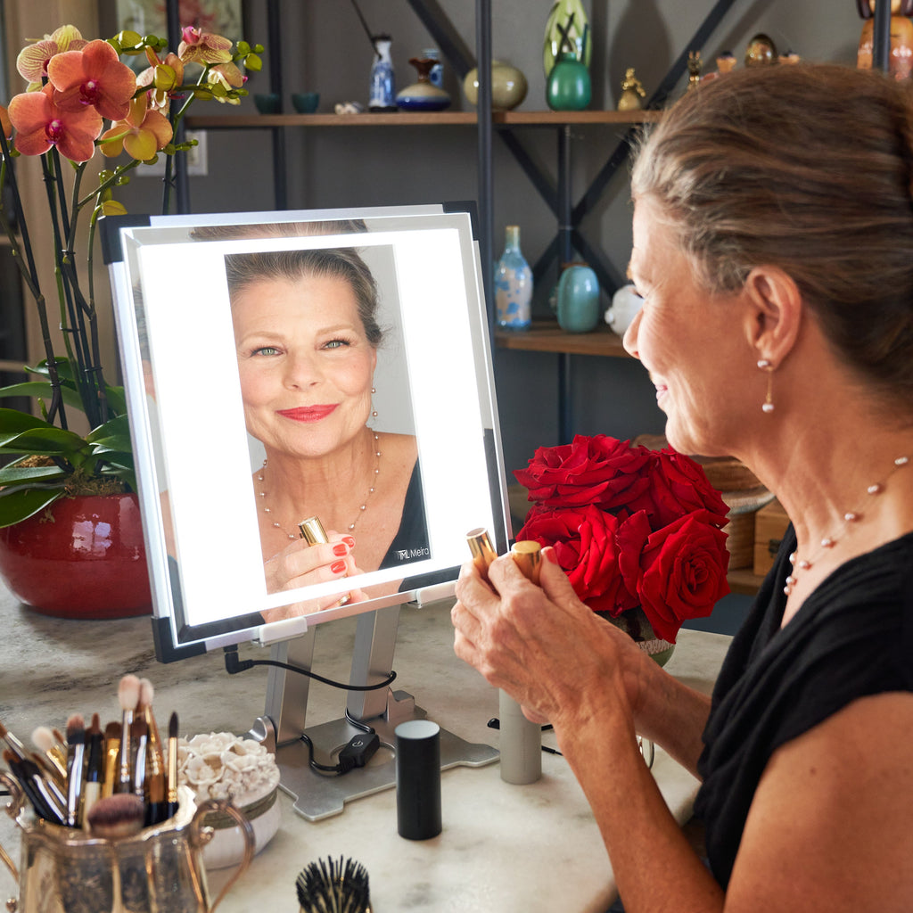 A beautiful, older woman regards her reflection in her TML Meira makeup vanity