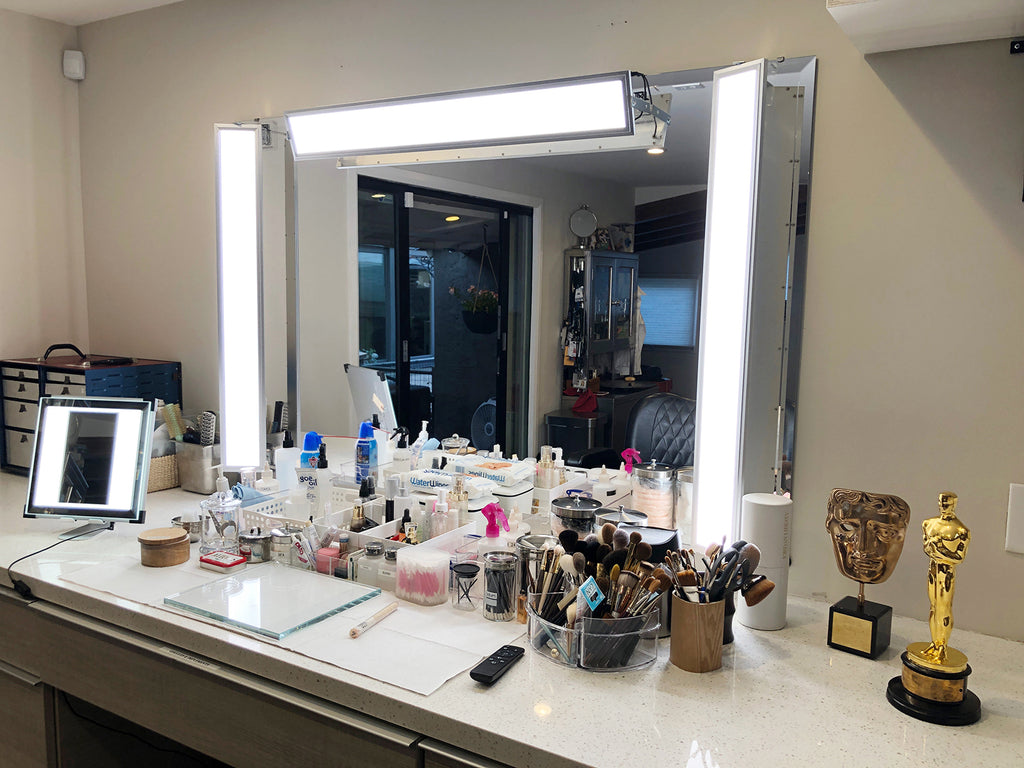 A custom makeup light set up with three panels surrounding the sides and top of a large mirror with makeup tools in front. A TML Meira to the left and a BAFTA and Academy Award to the right
