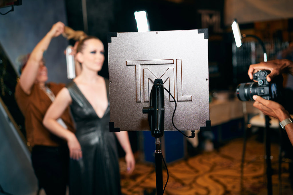 A photographer setting up a camera as a hair artist adjust a model in front of The Makeup Light lighting