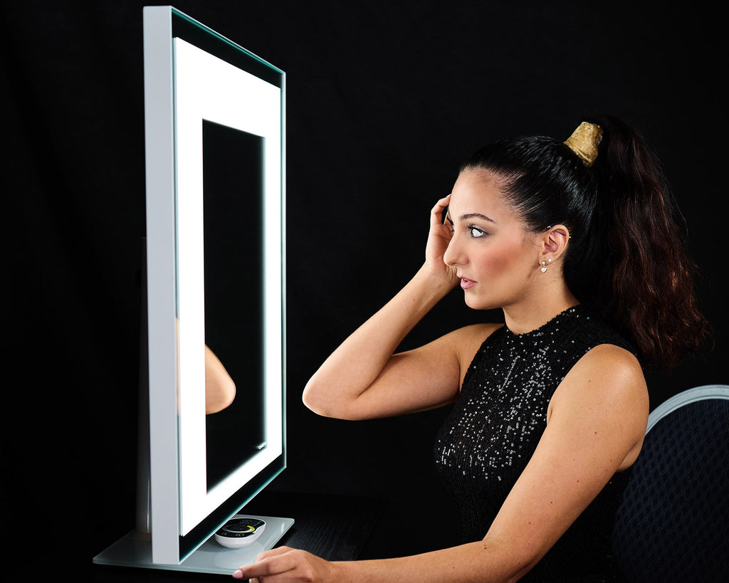 A woman in profile regards her reflection as she adjusts her hair.