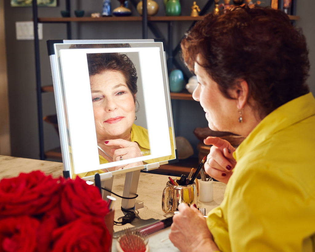 An ageless beauty regards her reflection in a TML Meira tabletop vanity. Red Roses out of focus in the lefthand corner of the frame.